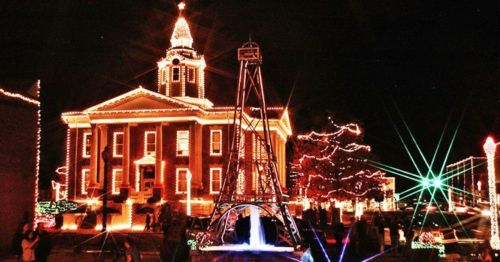 A festive town square at night, featuring a beautifully lit courthouse and holiday decorations.