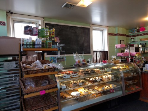 A cozy bakery interior featuring a display case filled with various pastries and treats, with shelves of goods in the background.