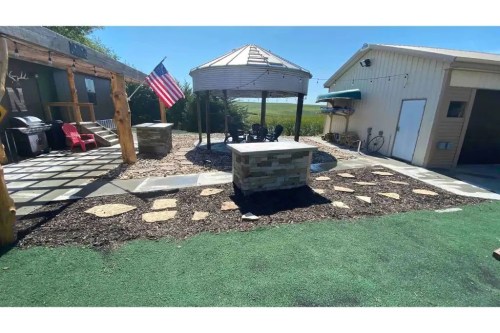 A backyard with a gazebo, stone pathway, American flag, and landscaped areas featuring grass and mulch.