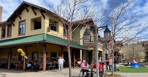 A charming building with a green roof, outdoor seating, and people enjoying a sunny day in a lively setting.