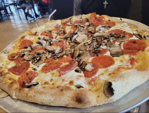 A large pizza topped with pepperoni, mushrooms, and melted cheese on a silver platter.