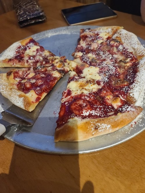 A pizza on a metal tray with slices topped with a sweet red sauce and powdered sugar.