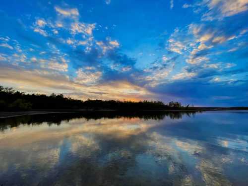 A serene landscape featuring a calm lake reflecting a vibrant sunset and colorful clouds against a blue sky.