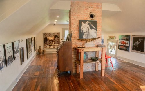 Art gallery interior featuring brick walls, wooden floors, and various artworks displayed on the walls.
