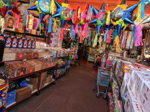 Colorful market aisle filled with festive decorations, snacks, and party supplies under a vibrant ceiling.