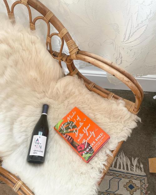 A cozy chair with a fluffy throw, a bottle of wine, and a colorful book resting on it.