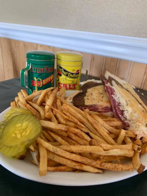 A plate of fries with a sandwich, pickles, and seasoning containers in the background.