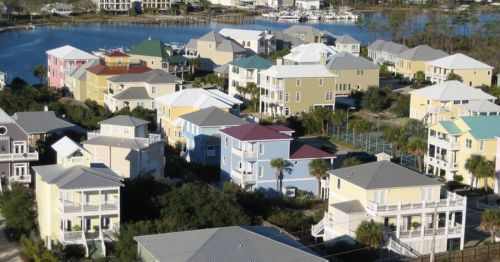 Aerial view of colorful houses near a calm water body, surrounded by trees and greenery.