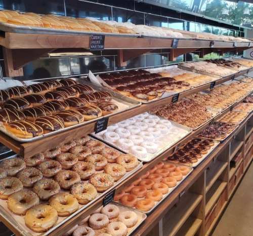 A display of various donuts on wooden shelves, featuring different toppings and flavors.