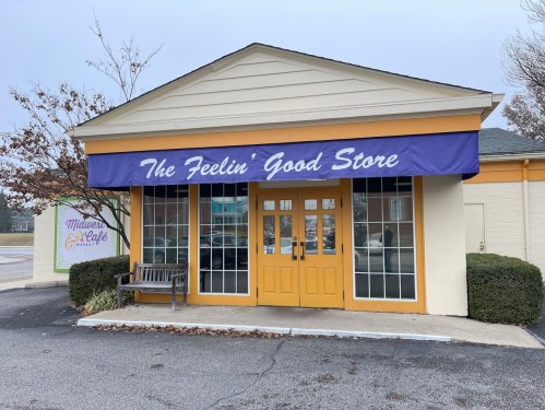 A storefront with a yellow door and windows, featuring a blue awning that reads "The Feelin' Good Store."