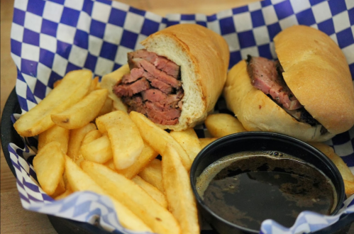 Two sandwiches filled with sliced meat, served with a side of golden fries and a small cup of dipping sauce.