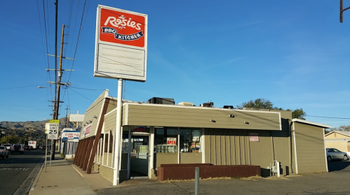 Exterior of Rosie's BBQ Kitchen, featuring a sign and a clear blue sky, located on a street with power lines.