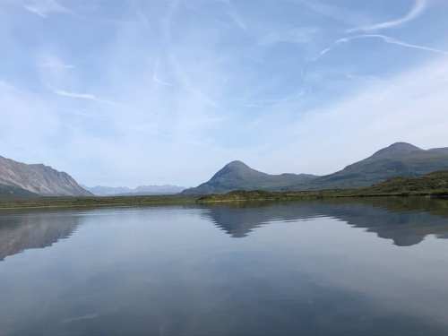 A serene landscape featuring a calm lake reflecting mountains under a clear blue sky.