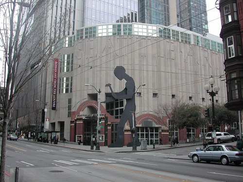 A large silhouette of a guitarist stands on the exterior of a building in an urban setting.