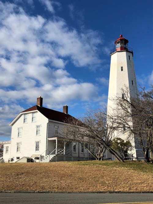A tall white lighthouse beside a historic white building, set against a blue sky with scattered clouds.