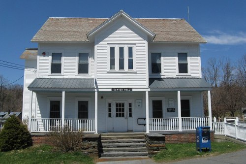 A white, two-story building with a porch and a blue mailbox in front, set against a clear blue sky.