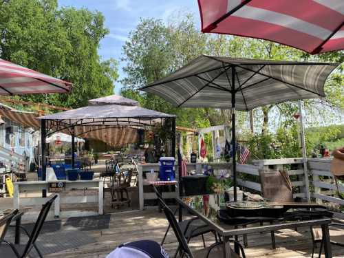 Outdoor seating area with umbrellas, tables, and a view of greenery and decorations in a relaxed, casual setting.