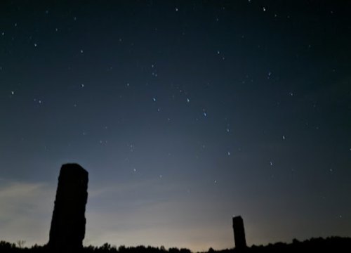 Silhouettes of stone structures against a starry night sky with a faint glow on the horizon.