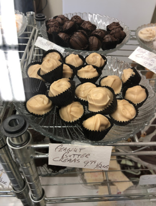 A display of peanut butter cream candies in black cups, alongside chocolate-covered treats on a wire rack.
