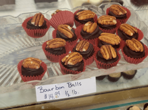 A display of bourbon balls topped with pecans, priced at $14.99 per half pound, in red paper cups.