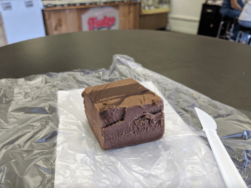A piece of chocolate fudge on a white napkin, resting on a black table with a plastic knife beside it.