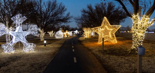 A pathway lined with large, illuminated holiday decorations, including stars and snowflakes, under a twilight sky.