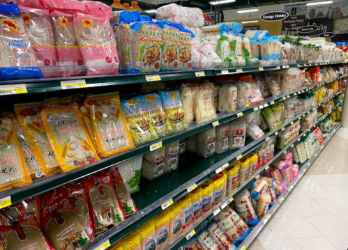 A grocery store aisle filled with various brands of rice and noodle packages on shelves.