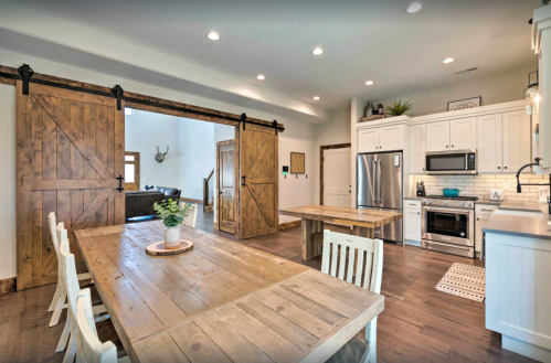 A modern kitchen with wooden accents, featuring a dining table, sliding barn doors, and stainless steel appliances.