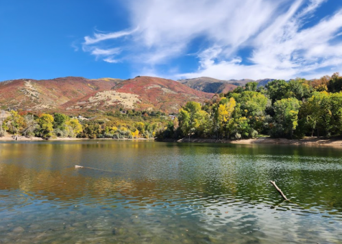 A serene lake surrounded by colorful autumn trees and mountains under a blue sky with wispy clouds.