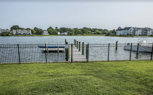 A serene waterfront view featuring a dock, boats, and a grassy area with a fence in the foreground.