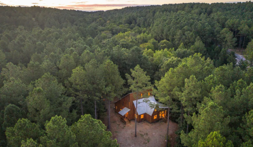 Aerial view of a cozy cabin nestled among dense green trees at sunset.