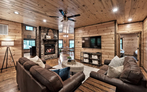 Cozy wooden living room with a fireplace, leather sofas, and a TV, featuring warm lighting and rustic decor.