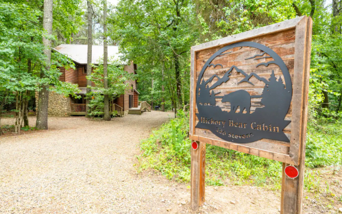 Sign for Hickory Bear Cabin in a wooded area, with a rustic cabin visible in the background.