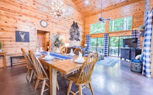 Cozy wooden dining area with a large table, rustic decor, and large windows overlooking a forested view.