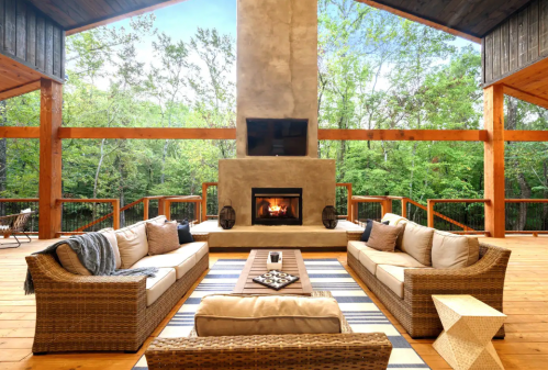 Cozy outdoor living space with a fireplace, comfortable seating, and a view of lush greenery.