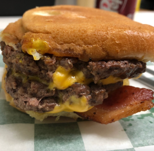 A close-up of a double cheeseburger with melted cheese and crispy bacon on a soft bun.