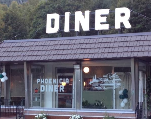 A cozy diner with a sign reading "Phoenicia Diner" and a classic car mural on the window, surrounded by greenery.