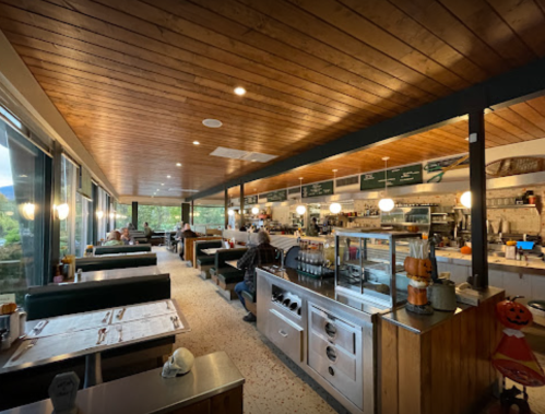 A cozy restaurant interior with wooden ceilings, booths, and a counter, featuring diners and a warm atmosphere.