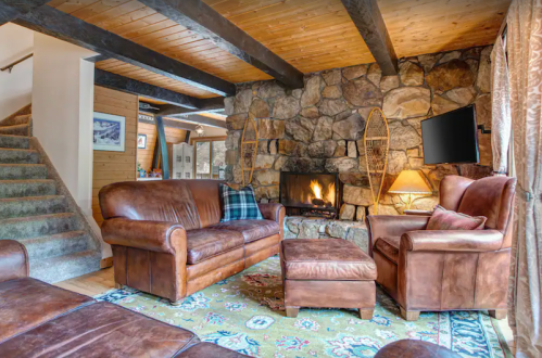 Cozy living room with leather sofas, a stone fireplace, and wooden beams, featuring a warm, inviting atmosphere.