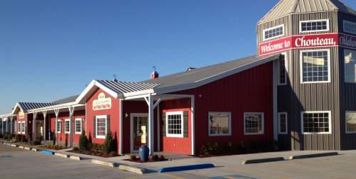 A red and gray building with a tower, featuring a sign that says "Welcome to Chouteau, Oklahoma." Clear blue sky.