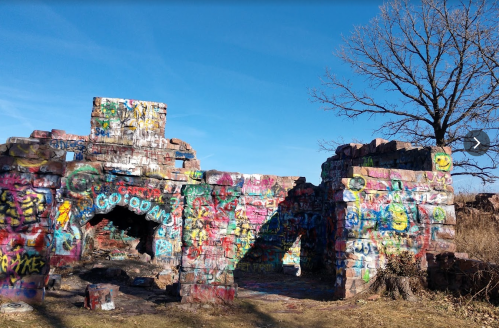Colorful graffiti covers the ruins of a stone structure, with a bare tree and clear blue sky in the background.