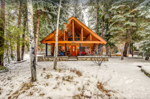 A cozy wooden cabin with a sloped roof, surrounded by snow-covered trees in a winter landscape.