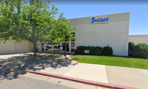 Exterior view of SeaQuest Interactive Aquarium, featuring a tree, grassy area, and a person walking by.