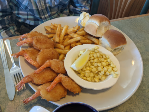 A plate with fried shrimp, French fries, corn, two dinner rolls, and a lemon wedge.