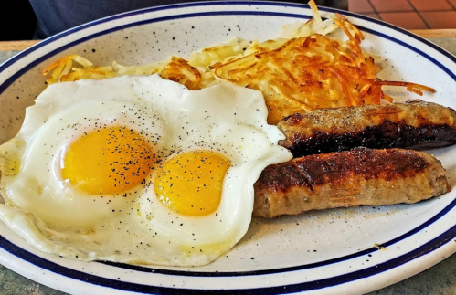 A plate of breakfast featuring two sunny-side-up eggs, sausage links, and crispy hash browns.