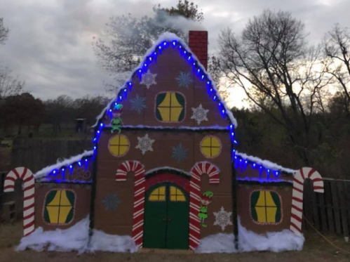 A festive gingerbread house decorated with candy canes, snowflakes, and blue lights against a cloudy sky.