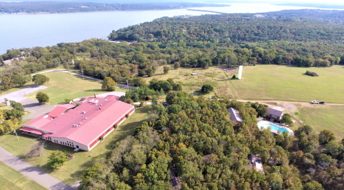Aerial view of a large building with a red roof surrounded by trees and a lake in the background.