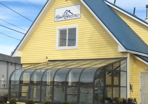 A yellow building with a blue roof and a glass-enclosed patio, featuring a sign that reads "Blue Reef Bistro."
