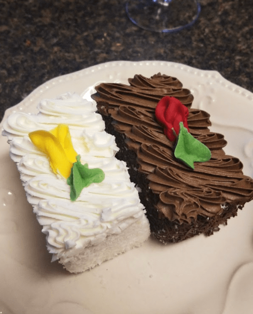Two small cakes on a plate: one white with yellow and green decorations, the other chocolate with red and green accents.