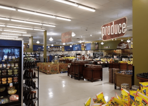 Interior of a grocery store featuring a produce section, shelves of snacks, and bright overhead lighting.